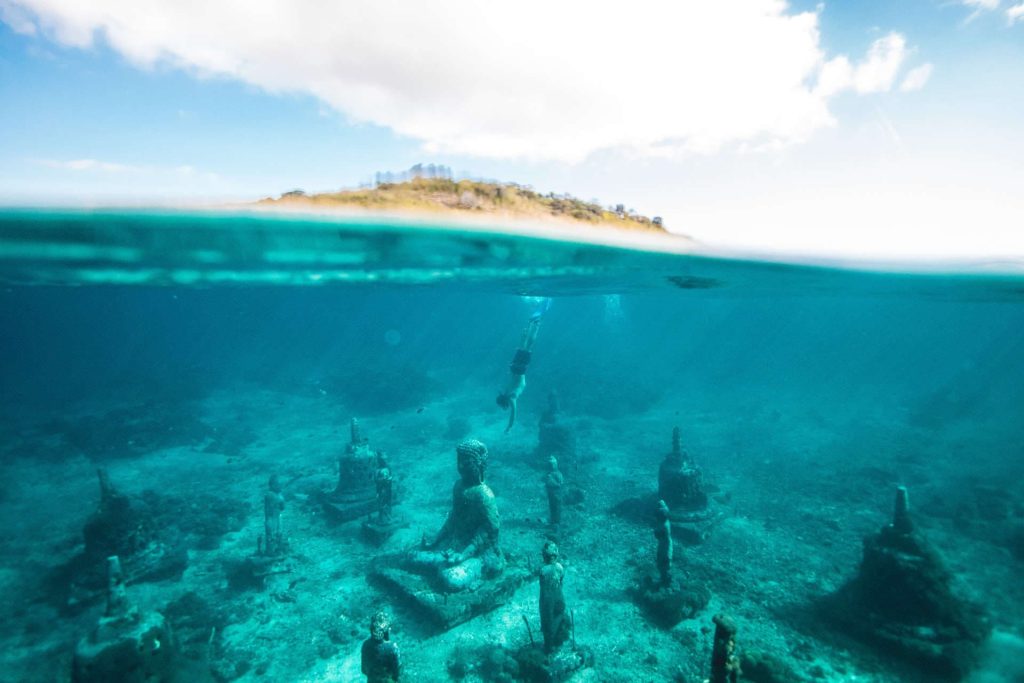 Freediver diving down to underwater statue