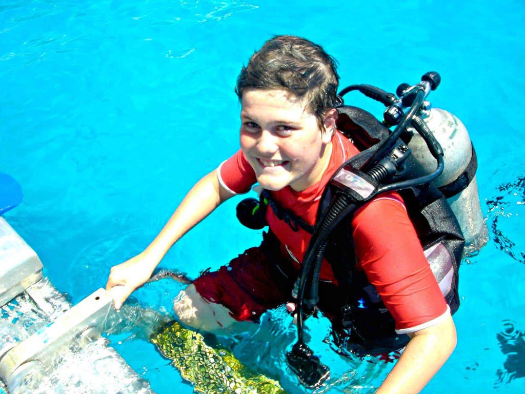 Scuba diving boy standing on pool ladder