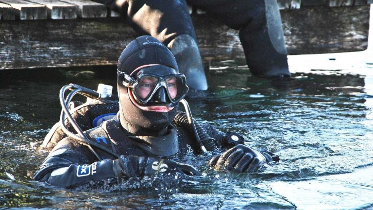 Scuba diver in drysuit diving in lake.