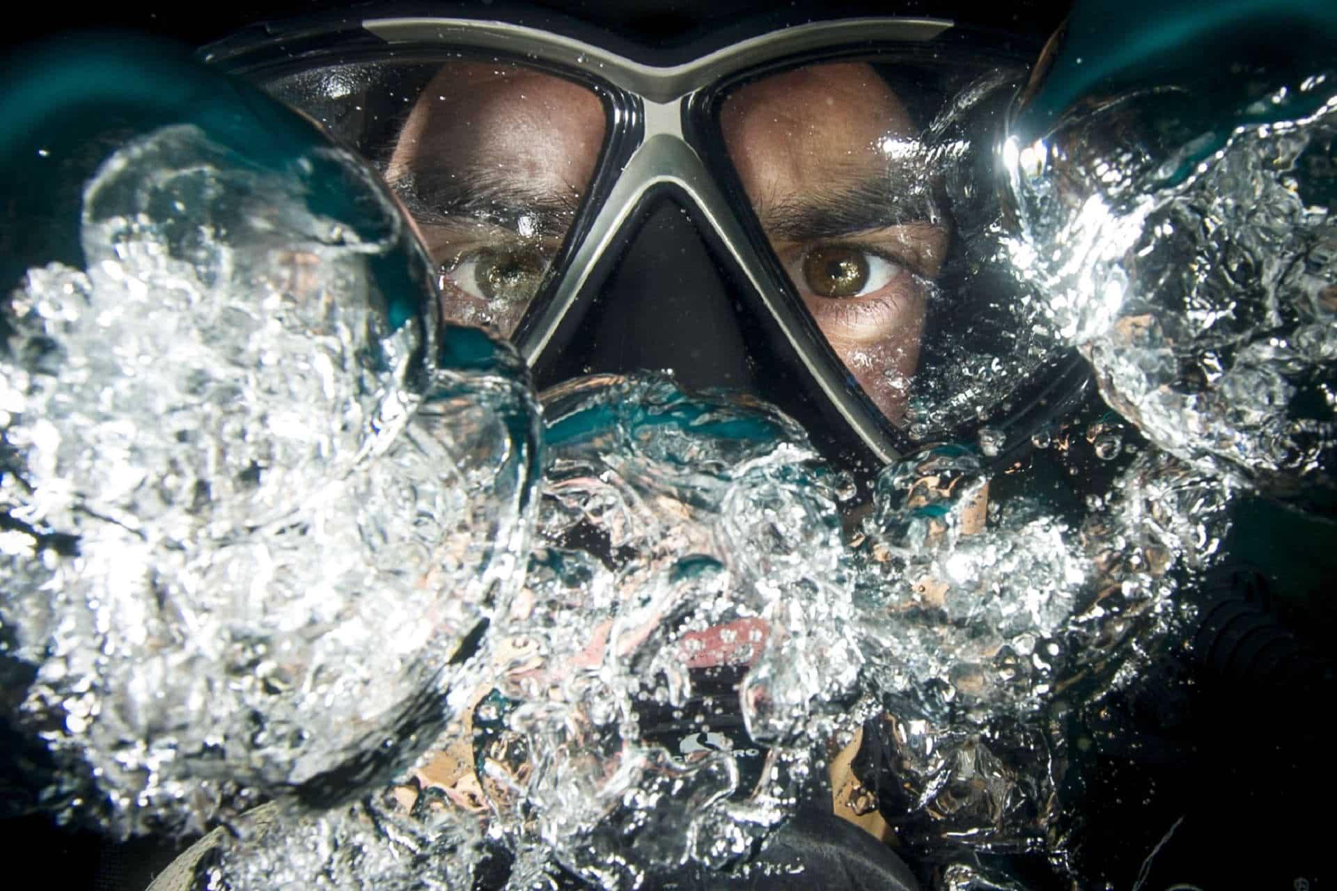 Scuba diver face behind mask blowing bubbles