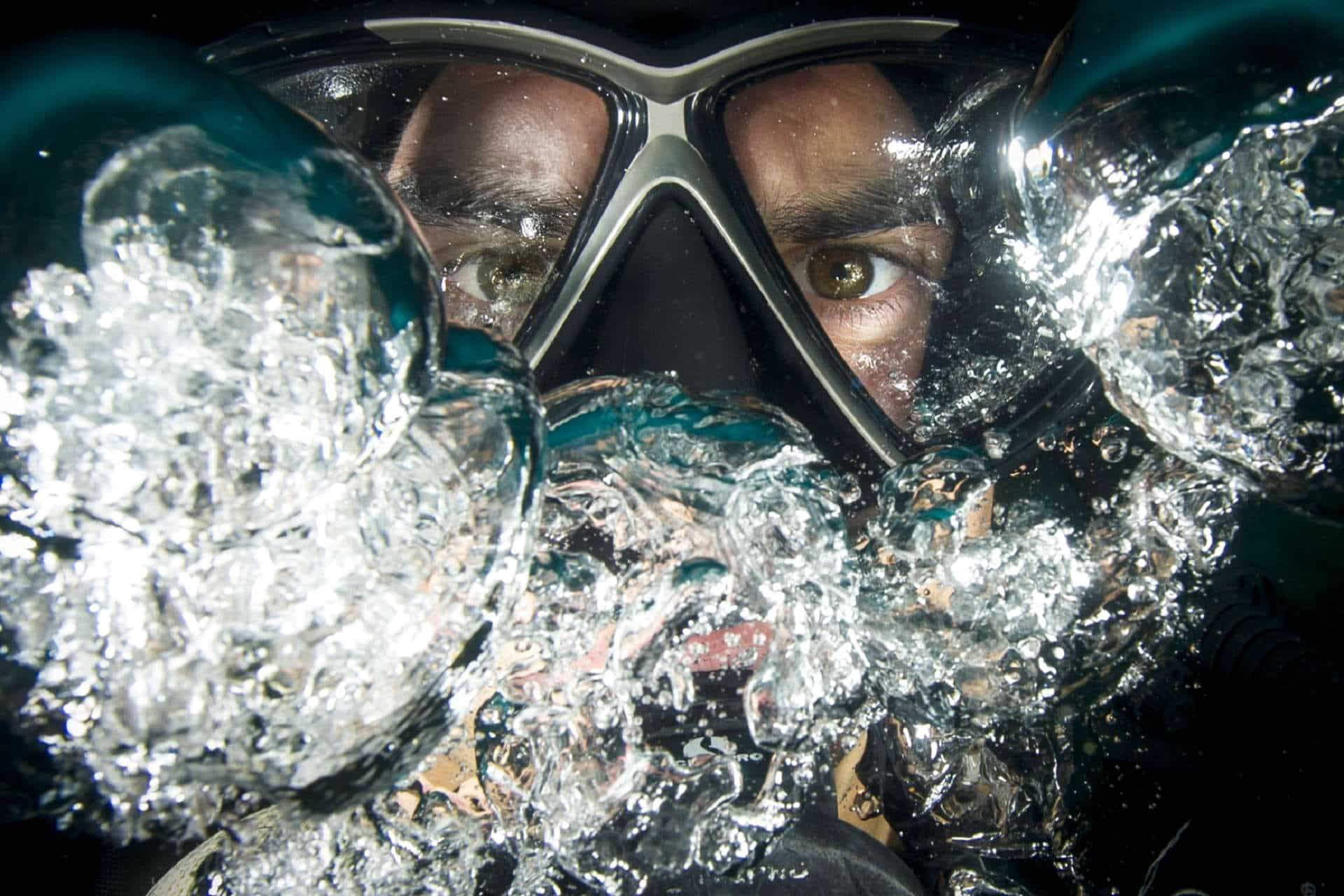 Taucher hinter Maske bläst Blasen ins Wasser