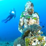 Scuba diver swimming besides statue underwater
