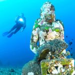 Taucher schwimmt unter Wasser an Statue vorbei