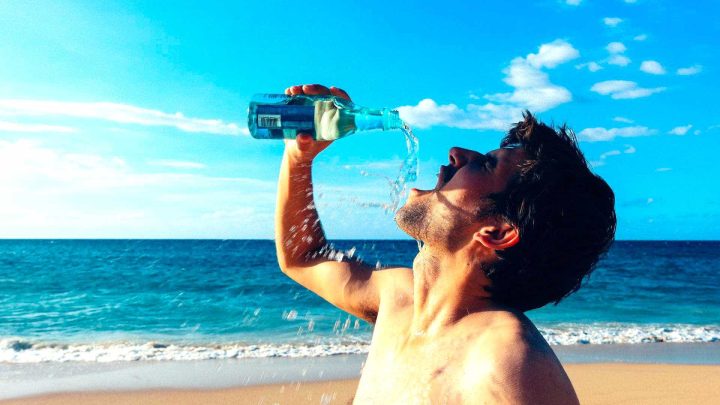 Mann trinkt Wasser am Strand