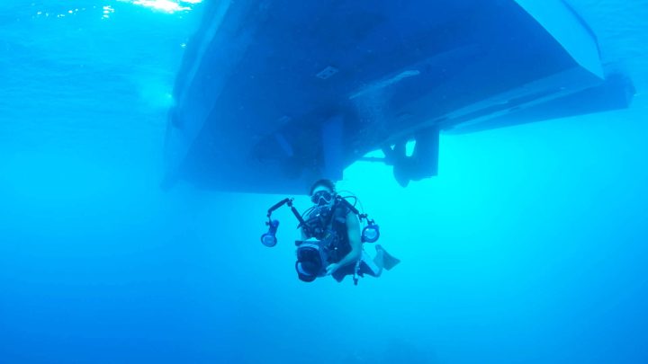 Underwater photographer scuba diving under boat.