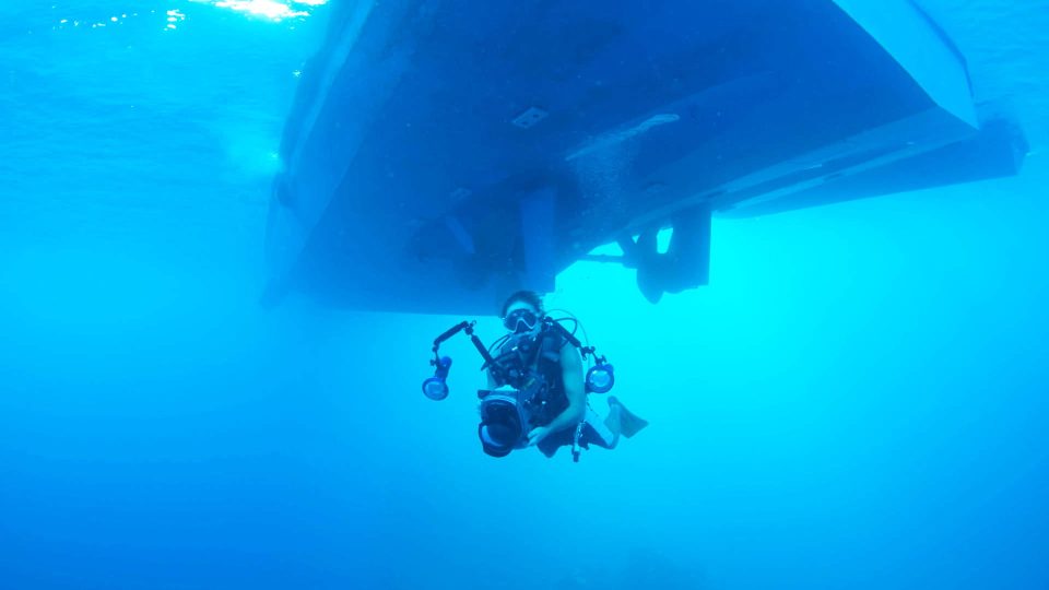 Underwater photographer scuba diving under boat